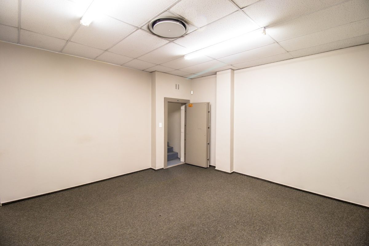 A clean, empty utility or storage room featuring a heavy-duty security door, suspended ceiling with fluorescent lighting, and carpeted flooring.