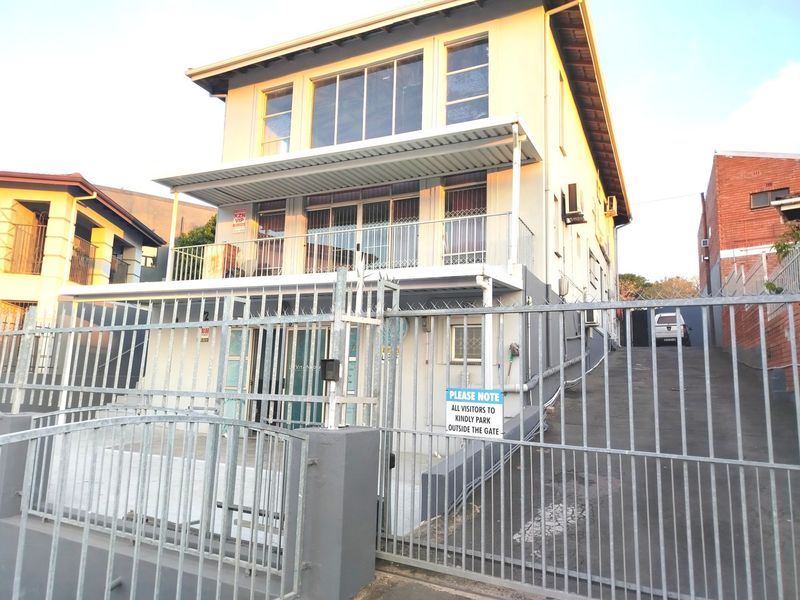 Front exterior view of a multi-story residential building featuring a metal security gate, driveway, and a balcony on the upper level.