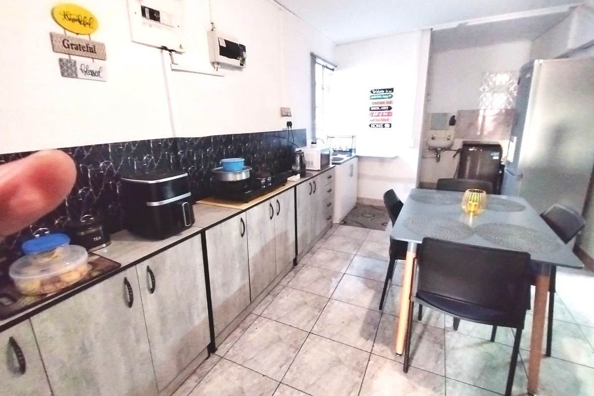 A functional kitchen featuring built-in cabinetry, tiled flooring, and a dark splashback, providing a practical workspace with an adjacent dining area.