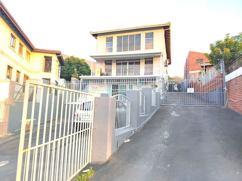 Front exterior view of a multi-story building featuring a gated driveway, paved access, and balcony areas with security fixtures.