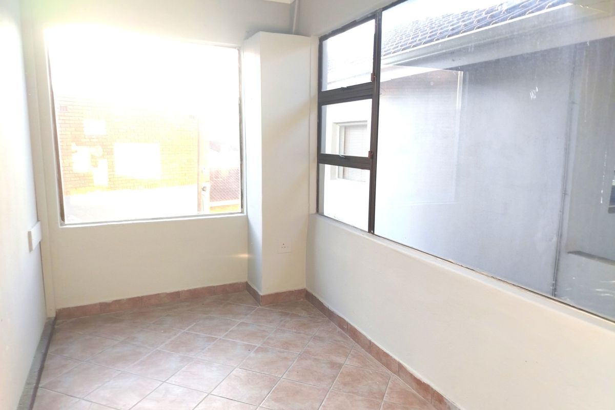 An empty, sunlit room featuring tiled flooring and large windows, offering a versatile space ready for personalization.