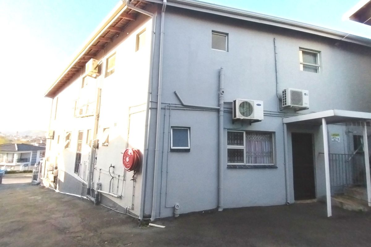 Rear exterior view of the property featuring paved ground, mounted air conditioning units, and a fire hose reel on the side wall.