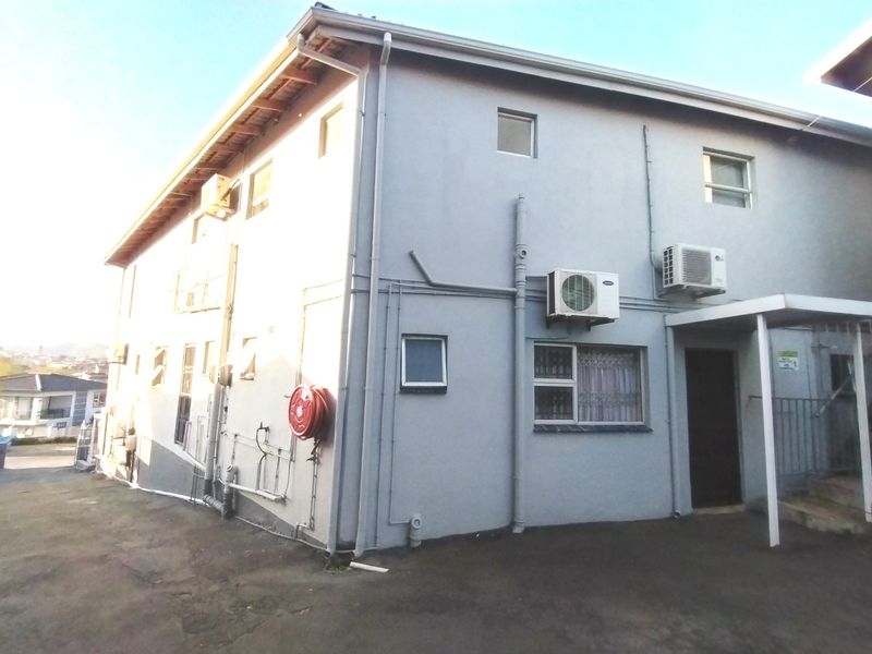 Rear exterior view of the property featuring paved ground, mounted air conditioning units, and a fire hose reel on the side wall.