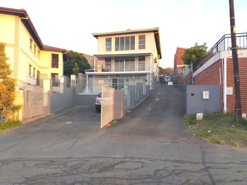 Front exterior view of a multi-level residential property featuring a paved driveway, secure metal gates, and boundary walls.