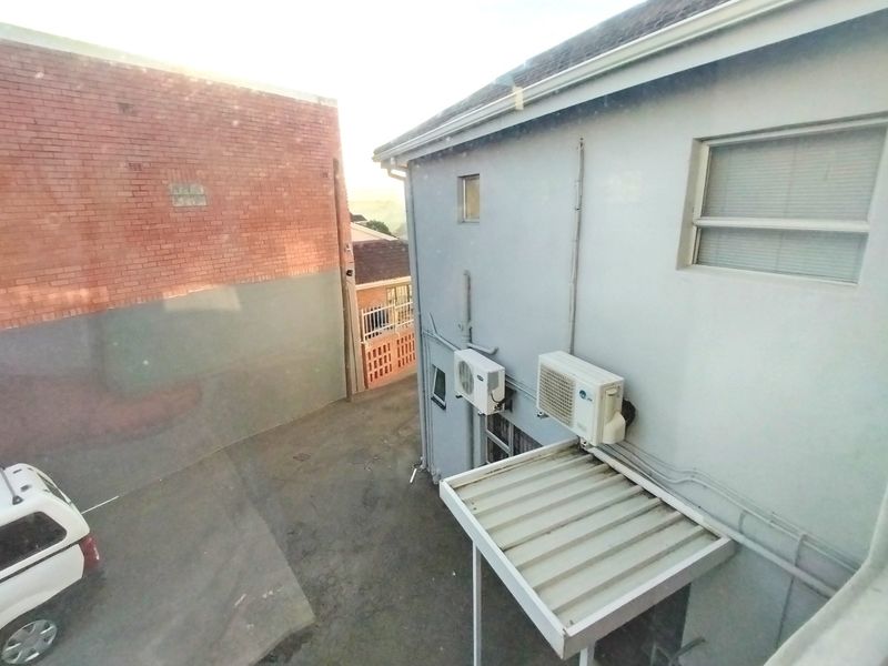 An elevated view of the rear exterior area showing a paved driveway, brick boundary wall, and mounted air conditioning units on the building facade.