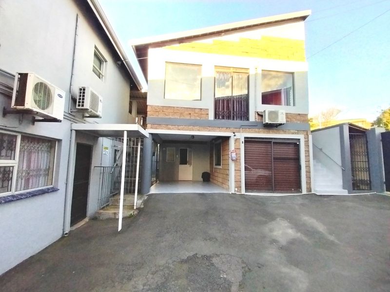 Front view of a multi-level residential property featuring a paved driveway, covered parking, garage, and external staircase access.