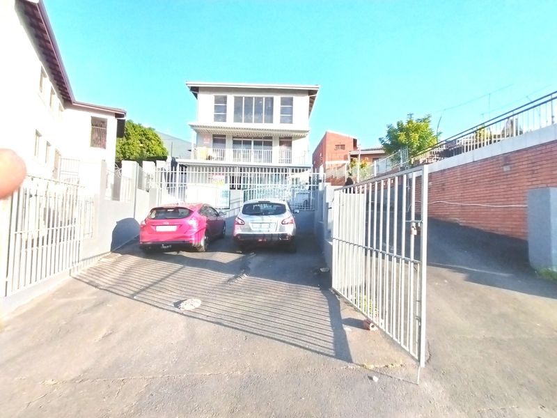 Front view of a multi-story residential property featuring a gated driveway, asphalt paving, and brick retaining walls.