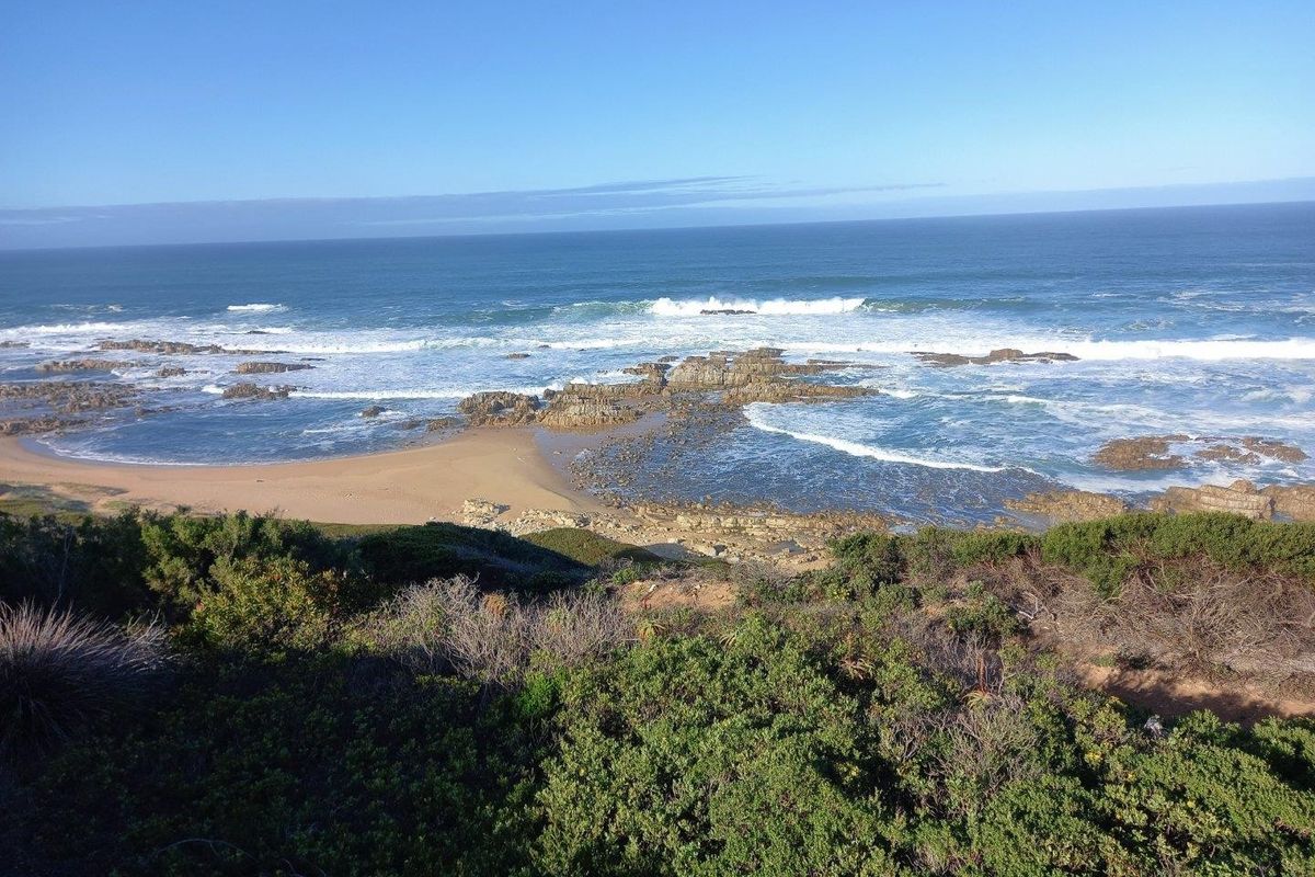 A scenic elevated view of the coastline featuring rocky outcrops, sandy beach, and ocean waves.