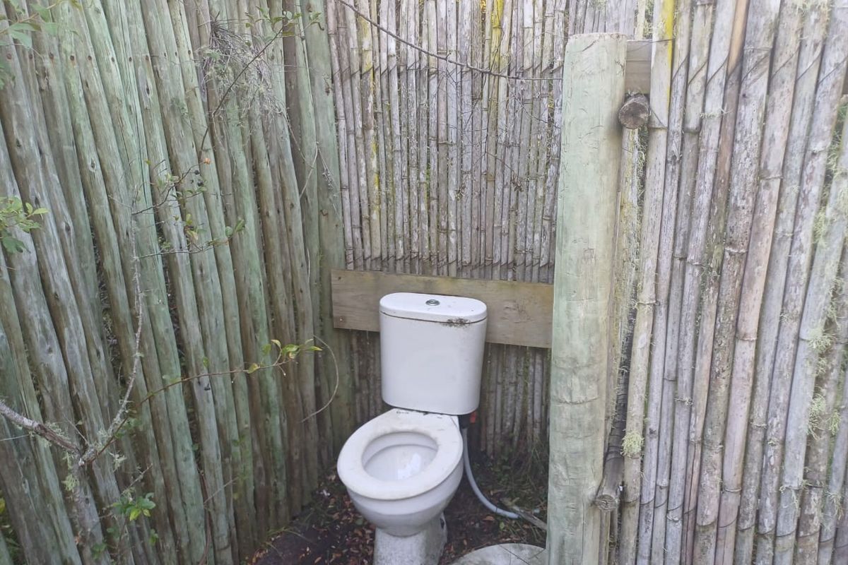 An outdoor toilet facility enclosed by weathered bamboo fencing, showing significant signs of wear and deterioration.