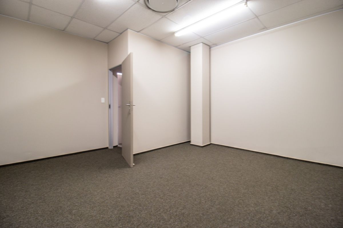 A clean, empty commercial office space featuring neutral walls, carpeted flooring, and a suspended ceiling with integrated lighting.