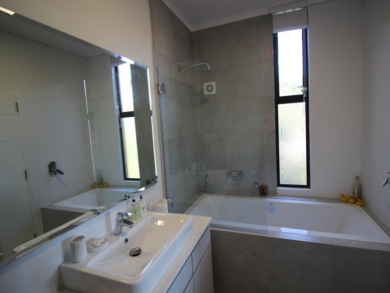 Modern bathroom featuring a built-in vanity with basin, a tiled bathtub with integrated shower screen, and large wall-mounted mirror.