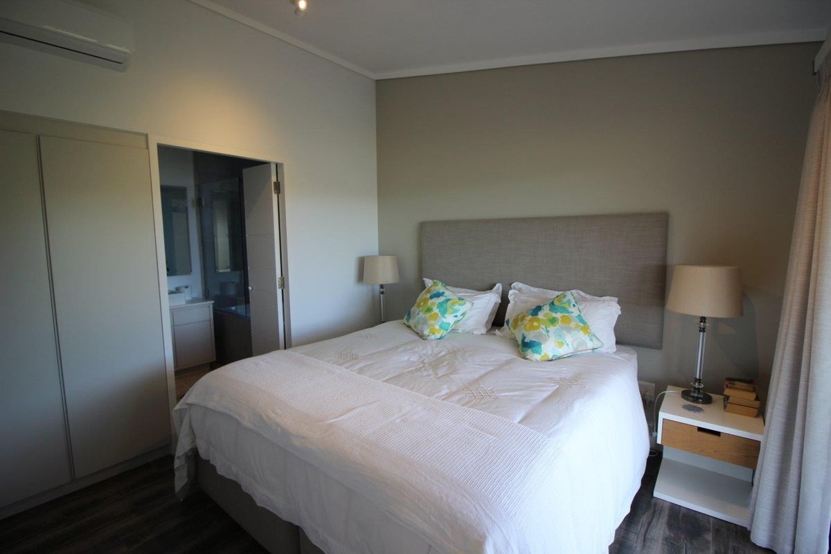 A well-maintained bedroom featuring laminate flooring, a built-in wardrobe, a wall-mounted air conditioning unit, and direct access to an en-suite bathroom.