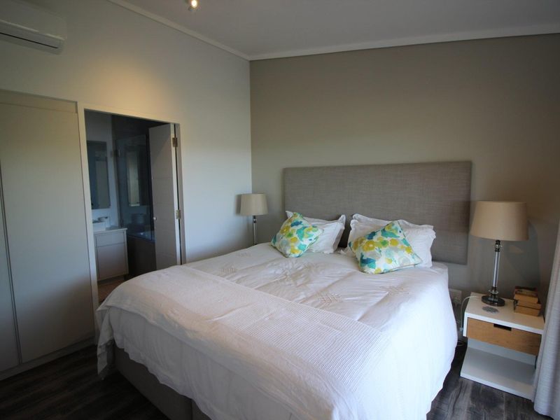A well-maintained bedroom featuring laminate flooring, a built-in wardrobe, a wall-mounted air conditioning unit, and direct access to an en-suite bathroom.