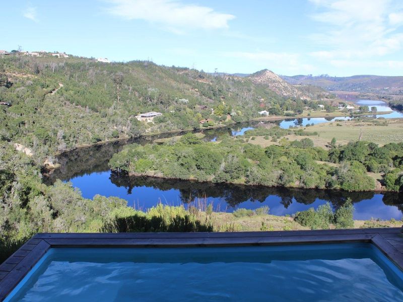 A scenic elevated view overlooking a winding river and lush landscape, featuring a foreground swimming pool with timber decking.