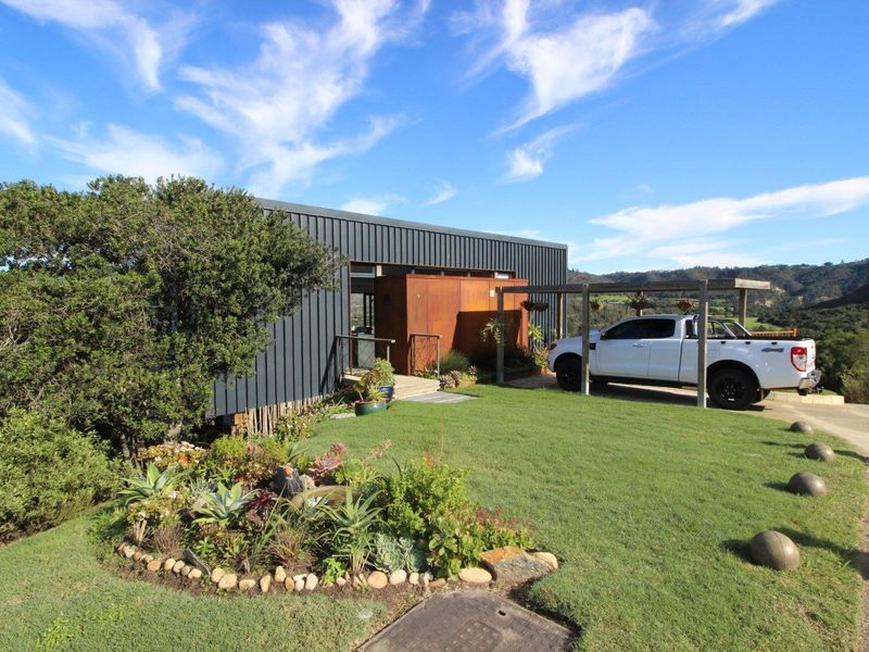 Modern home featuring dark metal cladding, a timber pergola, and a well-maintained landscaped garden with scenic rural views.