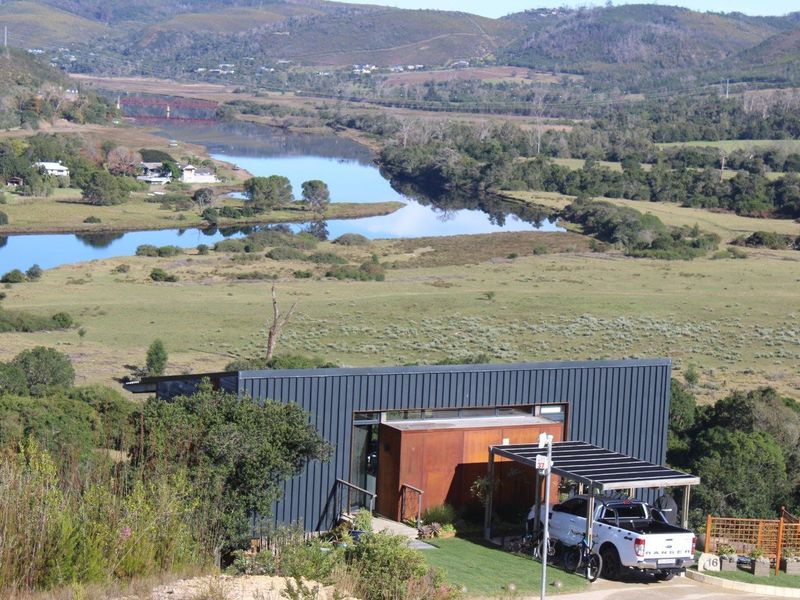 An elevated aerial view of a modern, metal-clad home set in a scenic landscape overlooking a river and valley.