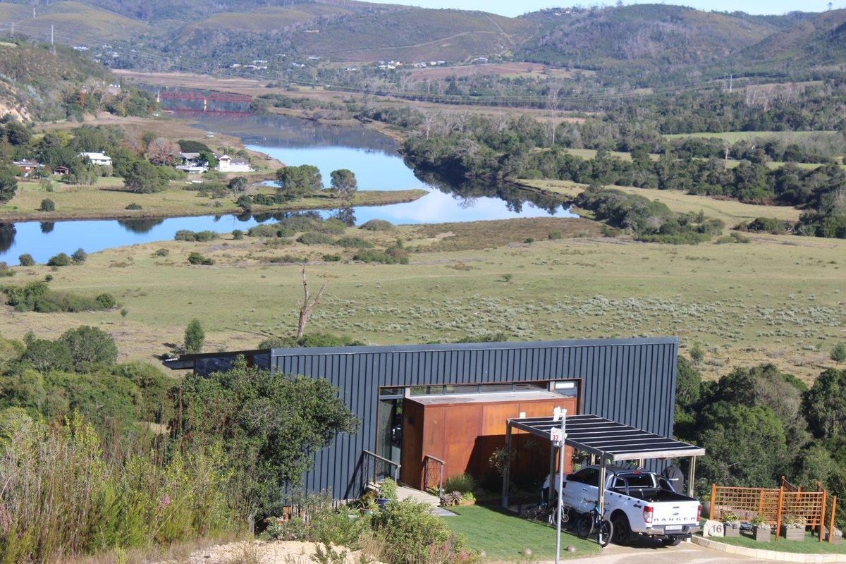 An elevated aerial view of a modern, metal-clad home set in a scenic landscape overlooking a river and valley.