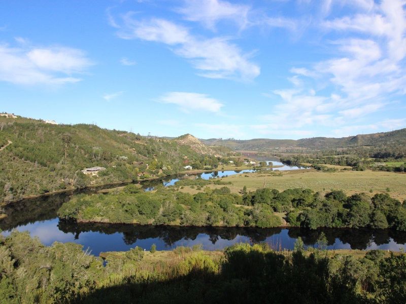 A scenic elevated view overlooking a winding river, lush green valley, and rolling hills under a clear blue sky.