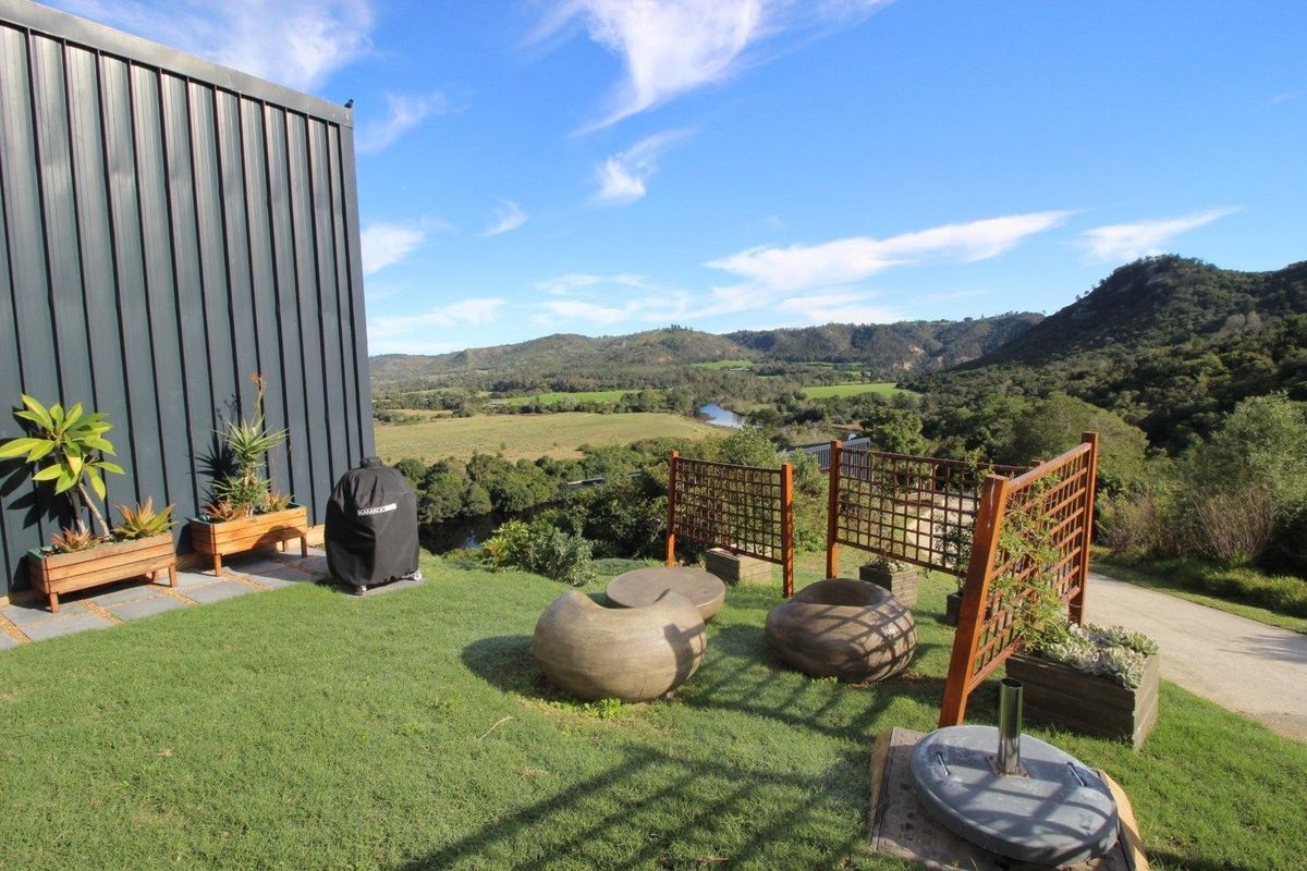 A rear garden area featuring modern metal cladding, timber lattice privacy screens, and expansive views over the surrounding valley and river landscape.