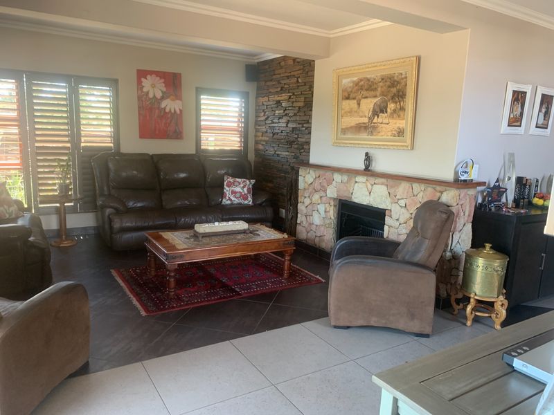 A comfortable living room featuring a prominent stone fireplace, a decorative stone feature wall, and tiled flooring with wooden window shutters.