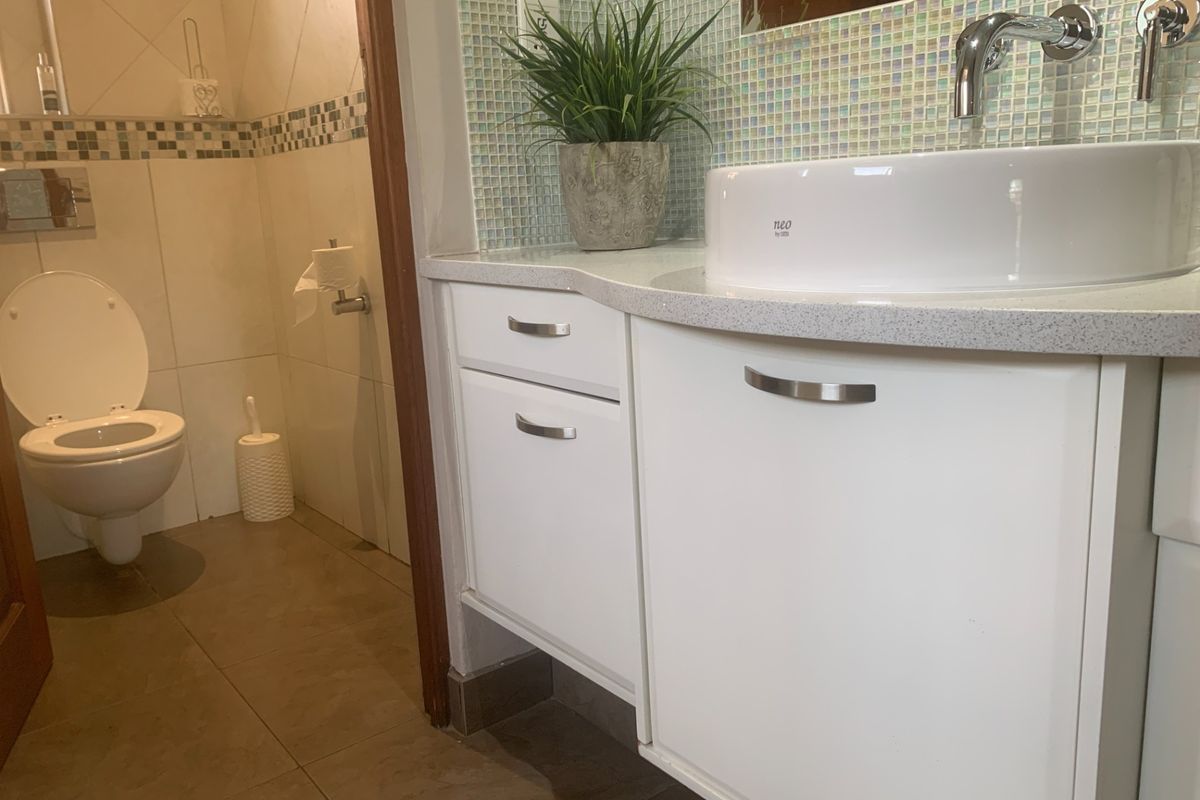 A modern bathroom featuring a white vanity with a vessel sink, mosaic tile backsplash, and a separate toilet area with tiled finishes.