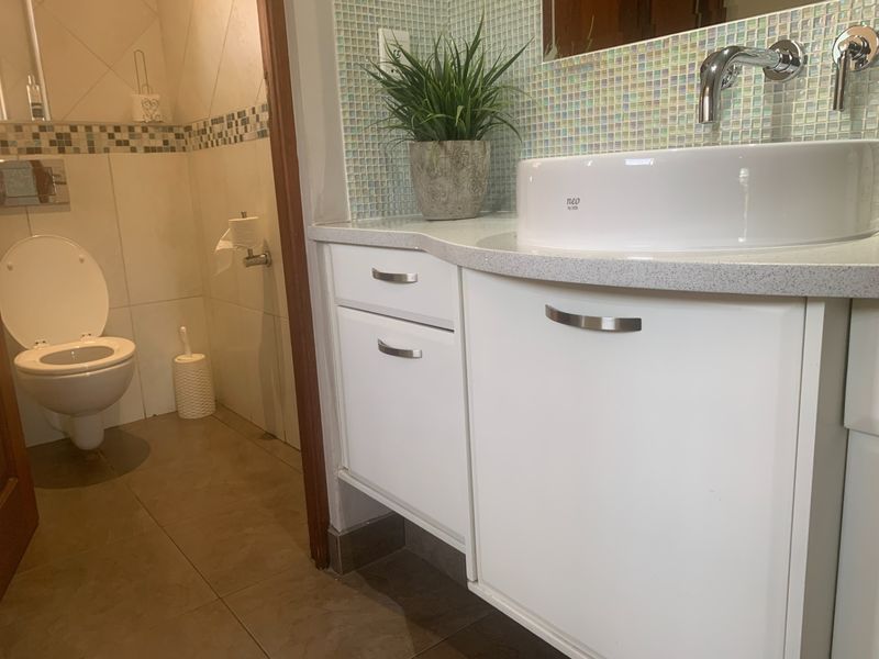 A modern bathroom featuring a white vanity with a vessel sink, mosaic tile backsplash, and a separate toilet area with tiled finishes.