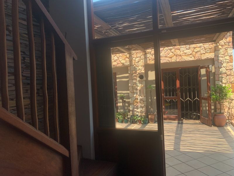 Entrance area featuring a wooden staircase and stone wall, opening onto a tiled patio with a thatched pergola and stone-clad exterior walls.