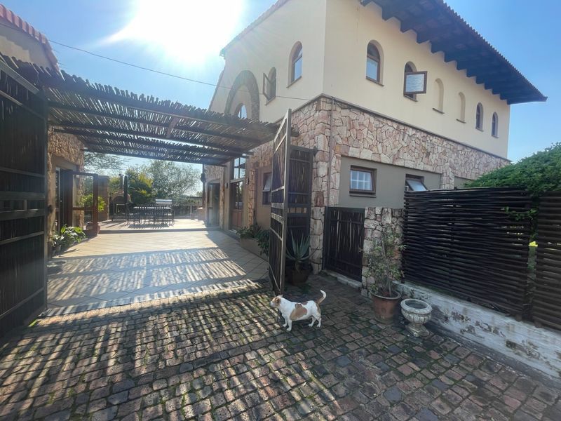 Rear exterior view featuring a stone-clad building, a covered patio area with a thatched pergola, and cobblestone paving.