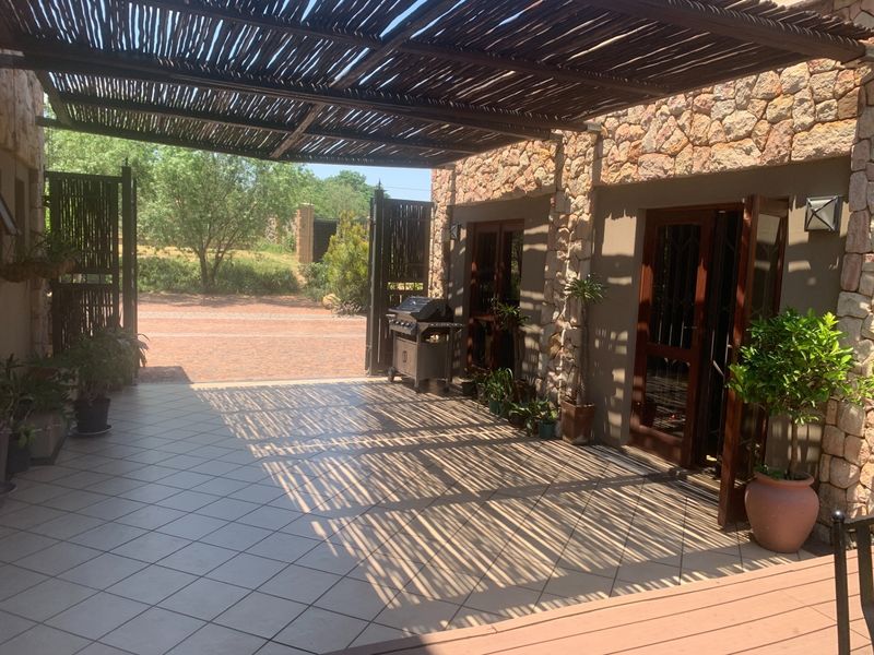 A spacious covered patio featuring a rustic thatched pergola, stone-clad walls, and tiled flooring, providing a seamless transition to the outdoor area.