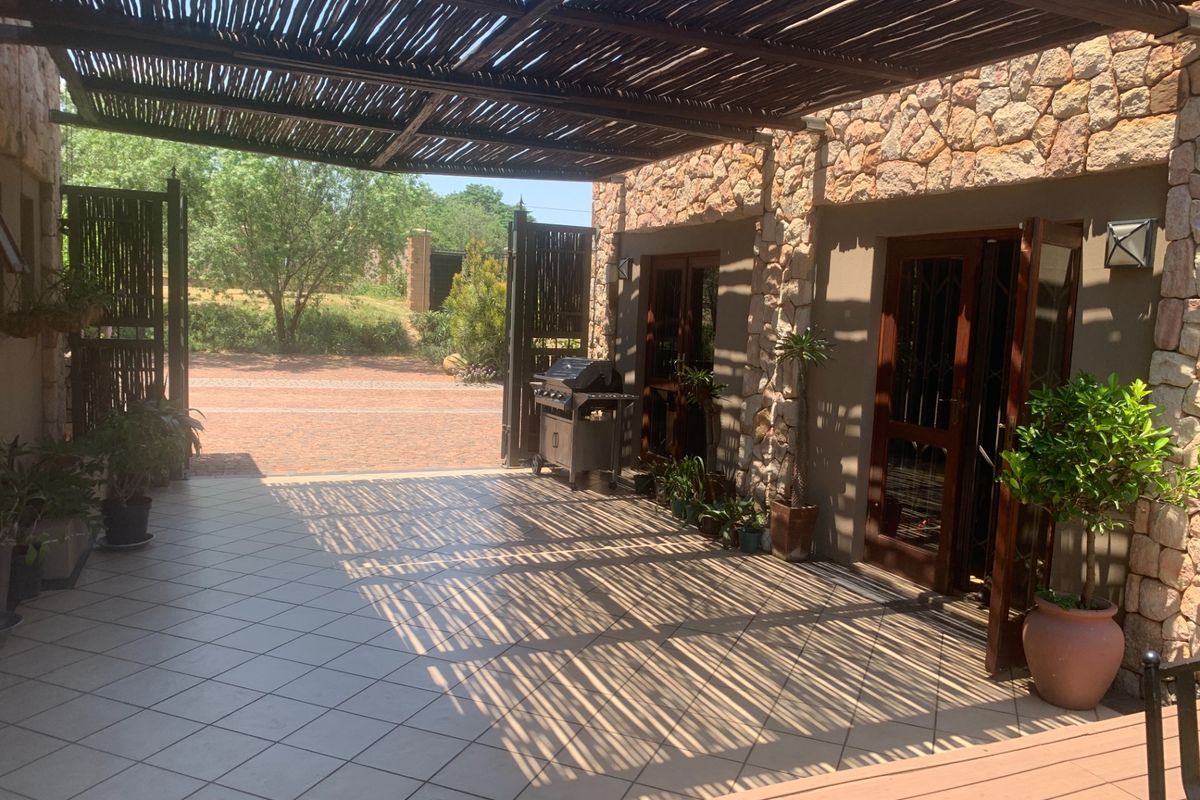 A spacious covered patio featuring a rustic thatched pergola, stone-clad walls, and tiled flooring, providing a seamless transition to the outdoor area.