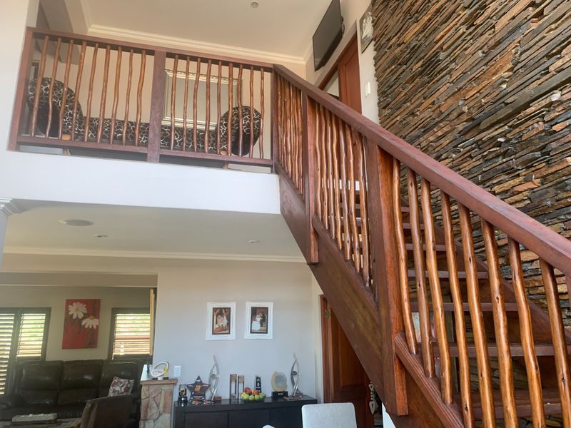 Spacious living area featuring a prominent wooden staircase, a striking stone feature wall, and an open mezzanine level overlooking the main floor.