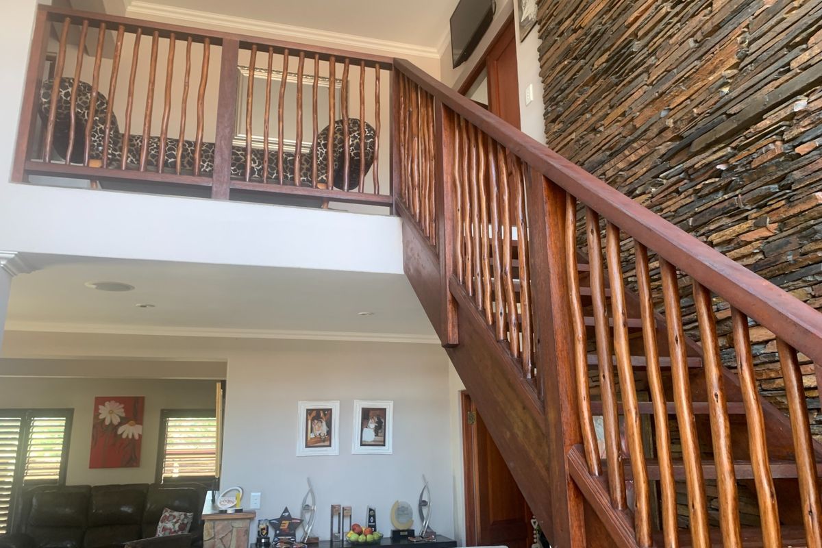 Spacious living area featuring a prominent wooden staircase, a striking stone feature wall, and an open mezzanine level overlooking the main floor.
