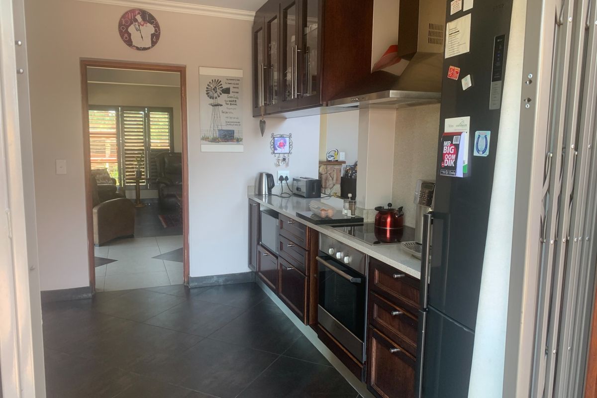 A functional kitchen featuring dark wood cabinetry, stone countertops, integrated oven and hob, and tiled flooring, with a view into the adjacent living area.