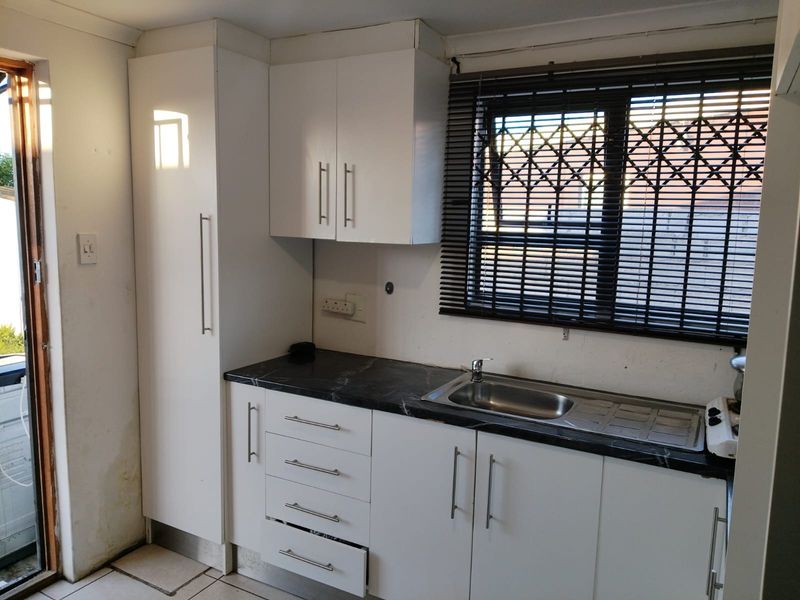 A functional kitchen featuring white cabinetry, dark laminate countertops, a stainless steel sink, and tiled flooring with direct access to the exterior.