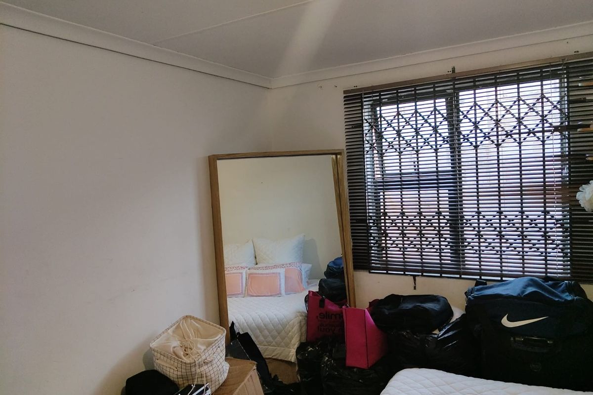 A bedroom featuring a window with a security gate and venetian blinds, providing natural light and essential security features.