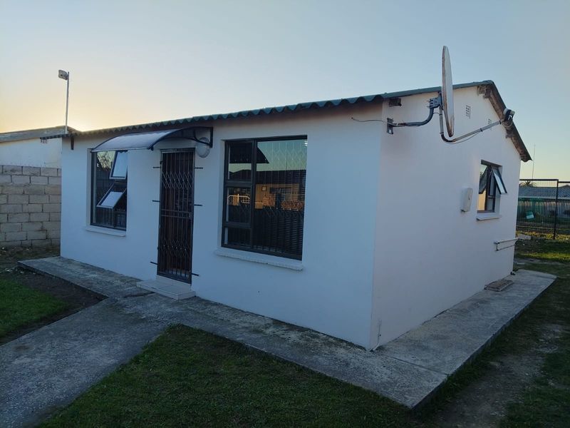 A view of the rear exterior of the house featuring white painted walls, security bars on windows, a security gate, and a concrete pathway.