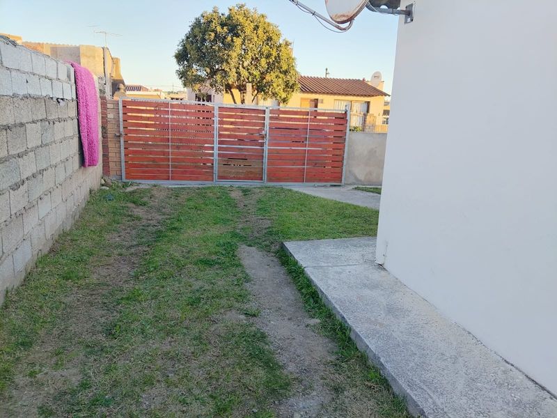 A rear outdoor area featuring a concrete pathway, a timber slat gate, and a boundary wall, offering potential for landscaping and garden improvement.