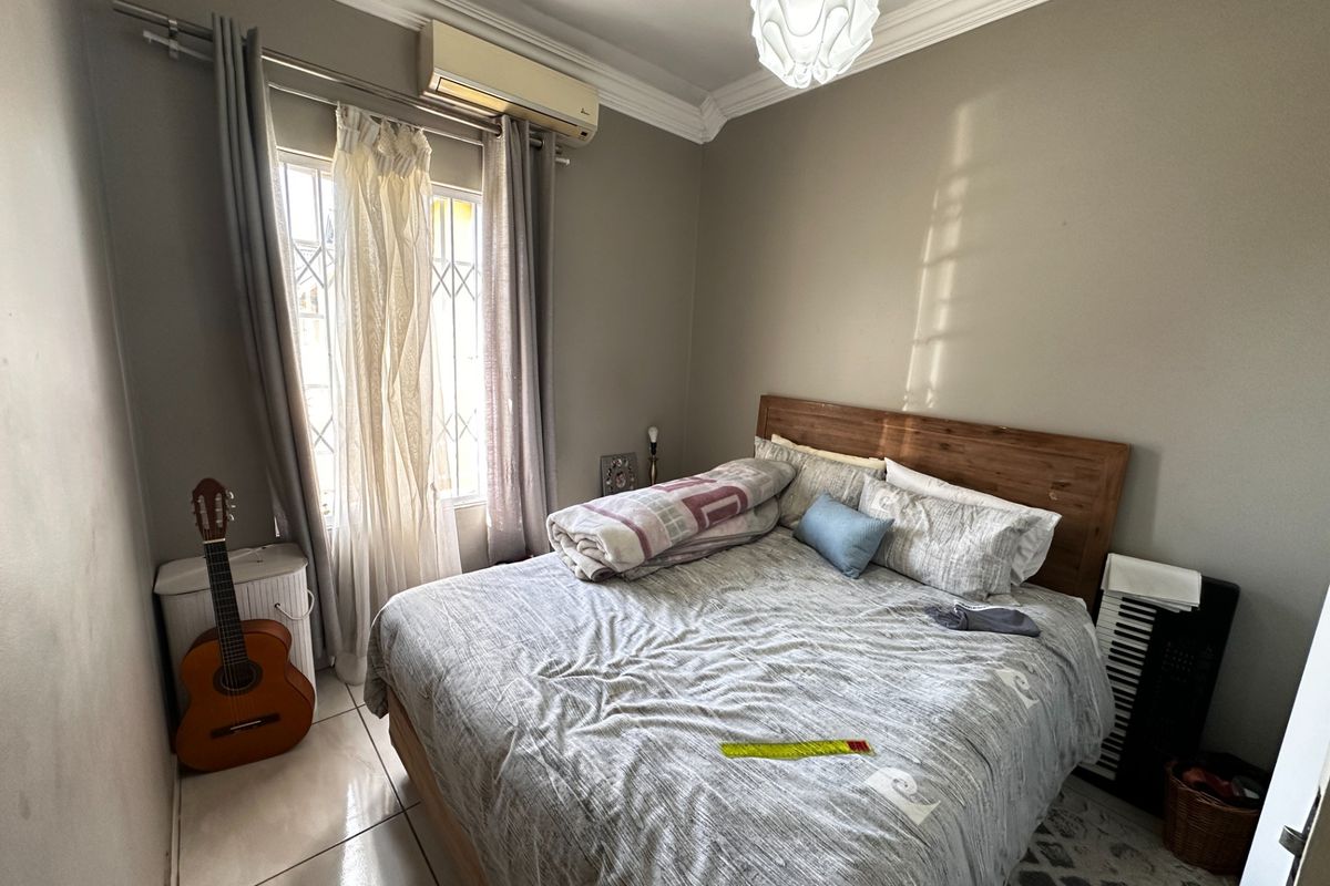 A bedroom featuring tiled flooring, crown molding, and a wall-mounted air conditioning unit, with security bars installed on the window.