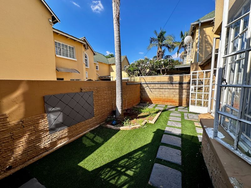A private rear courtyard featuring stone-clad boundary walls, artificial turf, and a stone-paved walkway leading to the townhouse entrance.