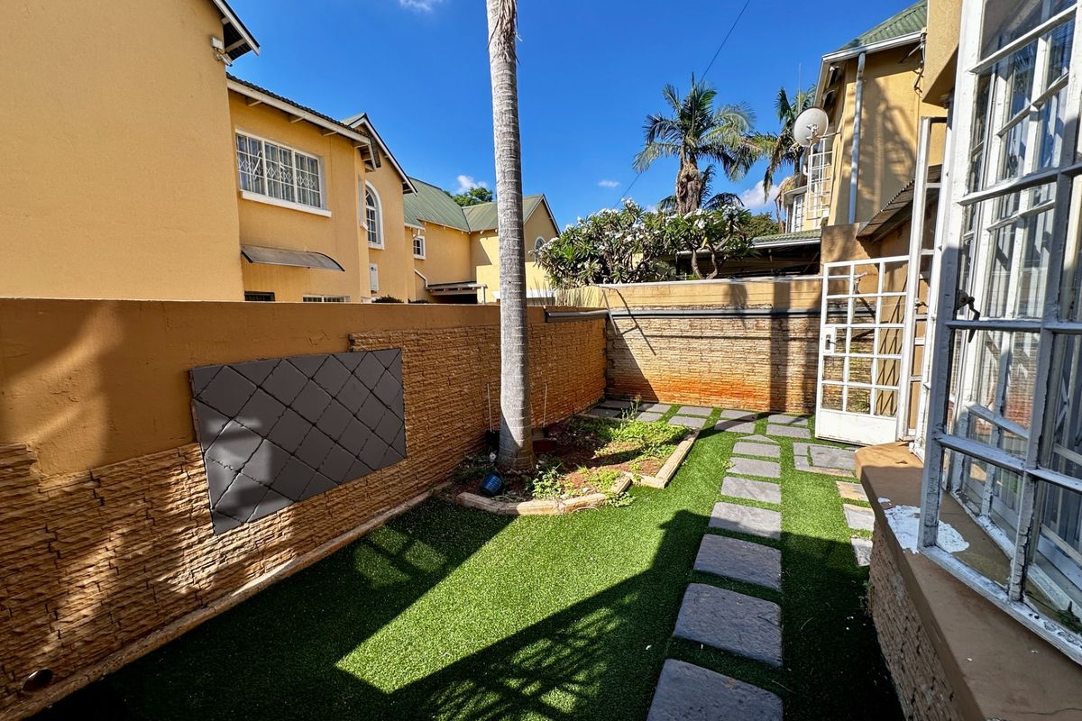 A private rear courtyard featuring stone-clad boundary walls, artificial turf, and a stone-paved walkway leading to the townhouse entrance.