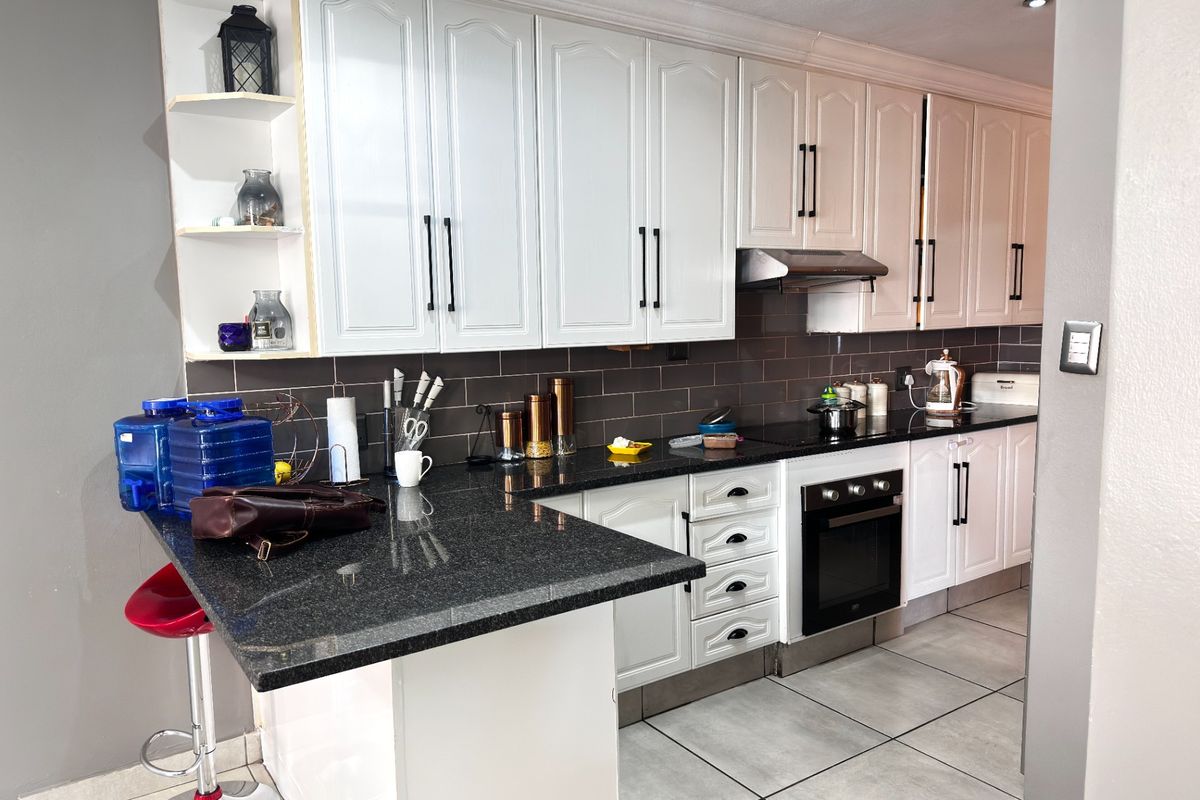 A functional kitchen featuring white cabinetry, dark granite countertops, a tiled backsplash, and a built-in oven with an extractor fan.