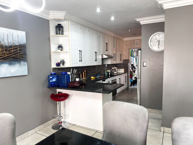 Open-plan kitchen featuring white cabinetry, granite countertops, and tiled flooring, seamlessly integrated with the dining area under modern recessed lighting.