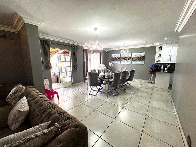 Spacious open-plan living and dining area featuring large format floor tiles, modern lighting, crown molding, and a seamless transition to the outdoor patio.