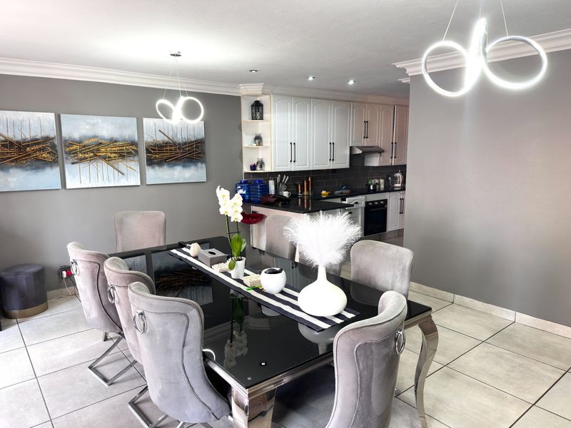 Open-plan dining area featuring modern tiled floors and contemporary lighting, seamlessly connected to a well-appointed kitchen with white cabinetry and dark countertops.