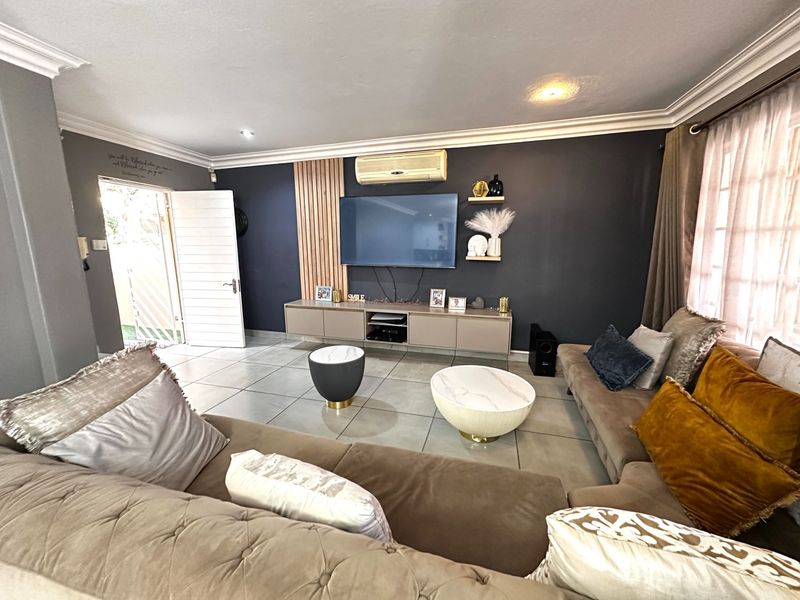 A modern living room featuring tiled floors, crown molding, and a feature wall with slatted wood paneling and a built-in media console.
