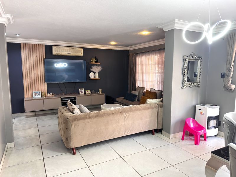 A well-maintained living room featuring tiled flooring, decorative timber wall paneling, built-in cabinetry, and a wall-mounted air conditioning unit.