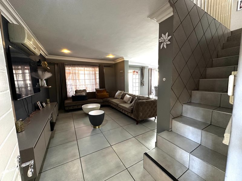 Spacious living room featuring large format floor tiles, a modern staircase with decorative wall paneling, and built-in cabinetry with integrated air conditioning.