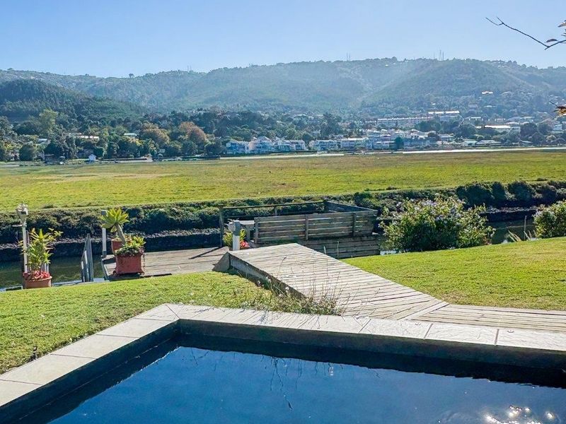 Outdoor pool area featuring stone coping, timber decking, and a private jetty overlooking a scenic landscape and river.