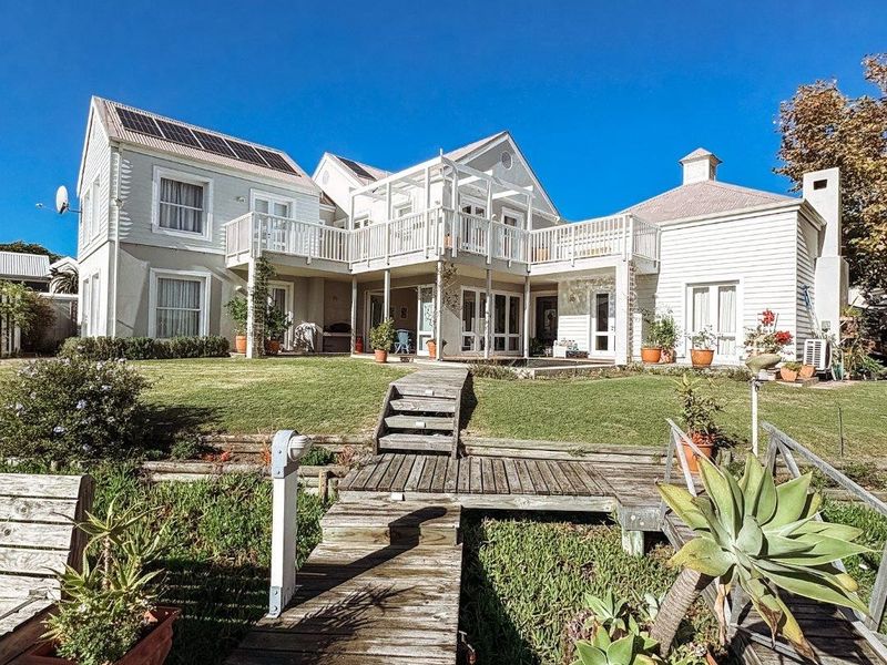 Rear view of a multi-level house featuring timber decking, a raised wooden walkway, and a balcony overlooking a landscaped garden area.