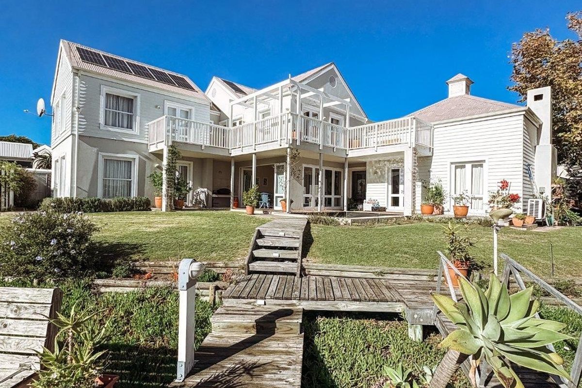 Rear view of a multi-level house featuring timber decking, a raised wooden walkway, and a balcony overlooking a landscaped garden area.